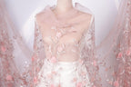 A mannequin wearing a white dress with pink floral embroidery and a sheer pink veil draped over it.