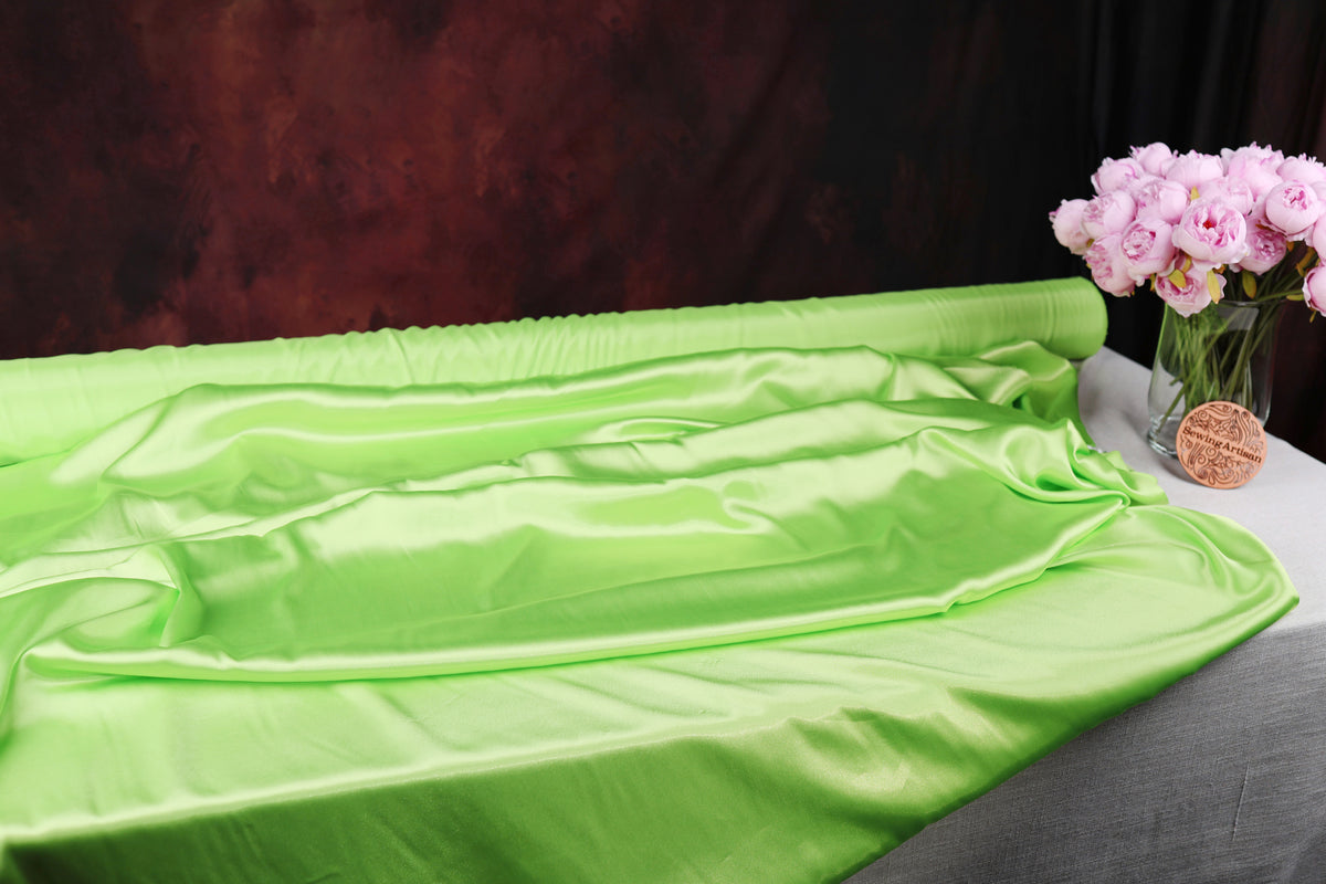a green satin fabric draped over a table, with a vase of pink flowers placed next to it.
