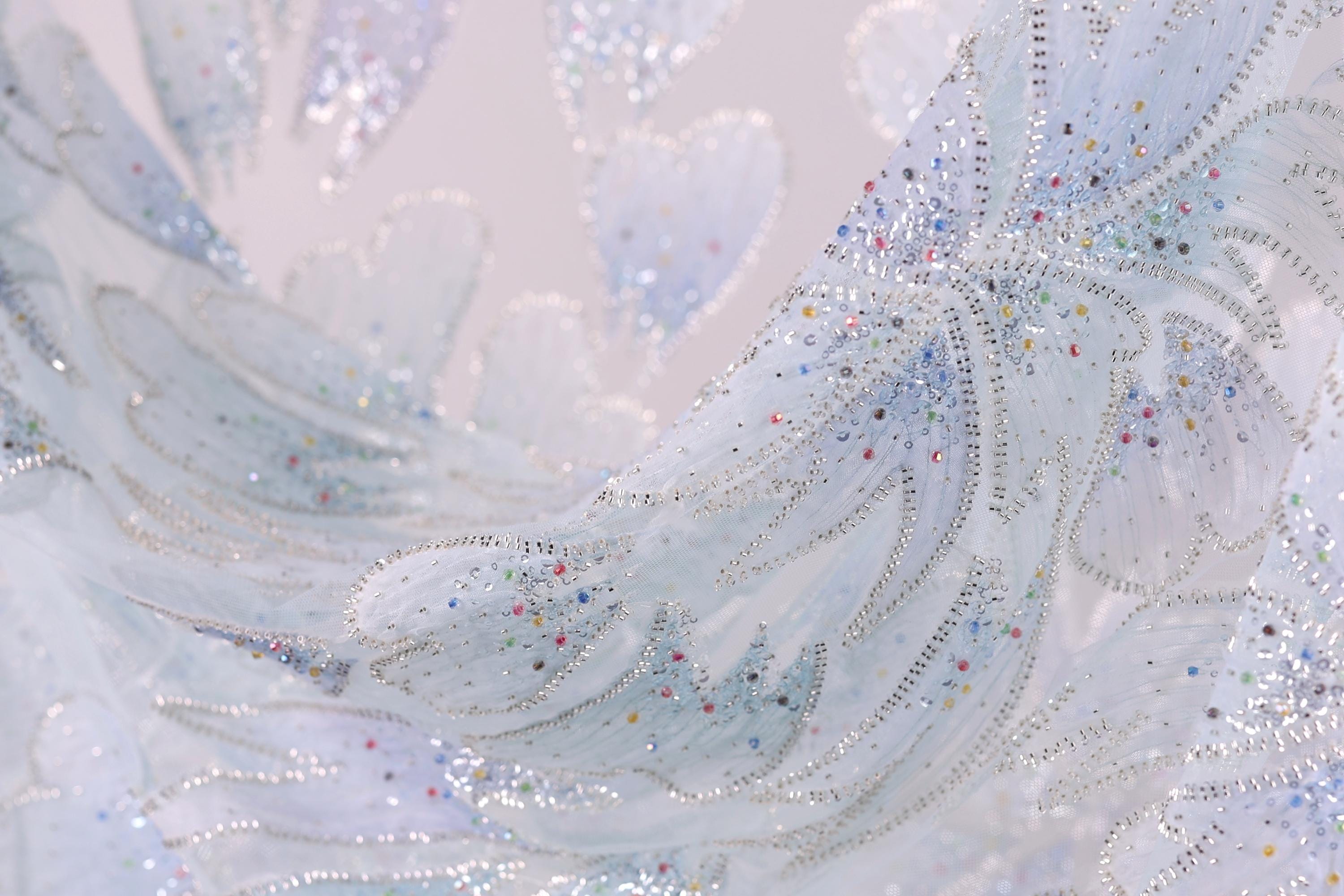 The image is a close-up of a fabric with a delicate, intricate design featuring a pattern of small, colorful dots and lines that create a sense of movement and texture.