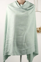 A light green, draped garment is displayed on a mannequin, with a blurred background.