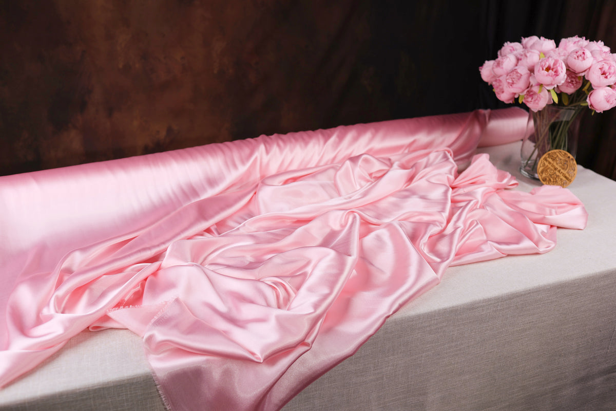 a pink satin fabric draped over a table, with a vase of pink flowers placed next to it.