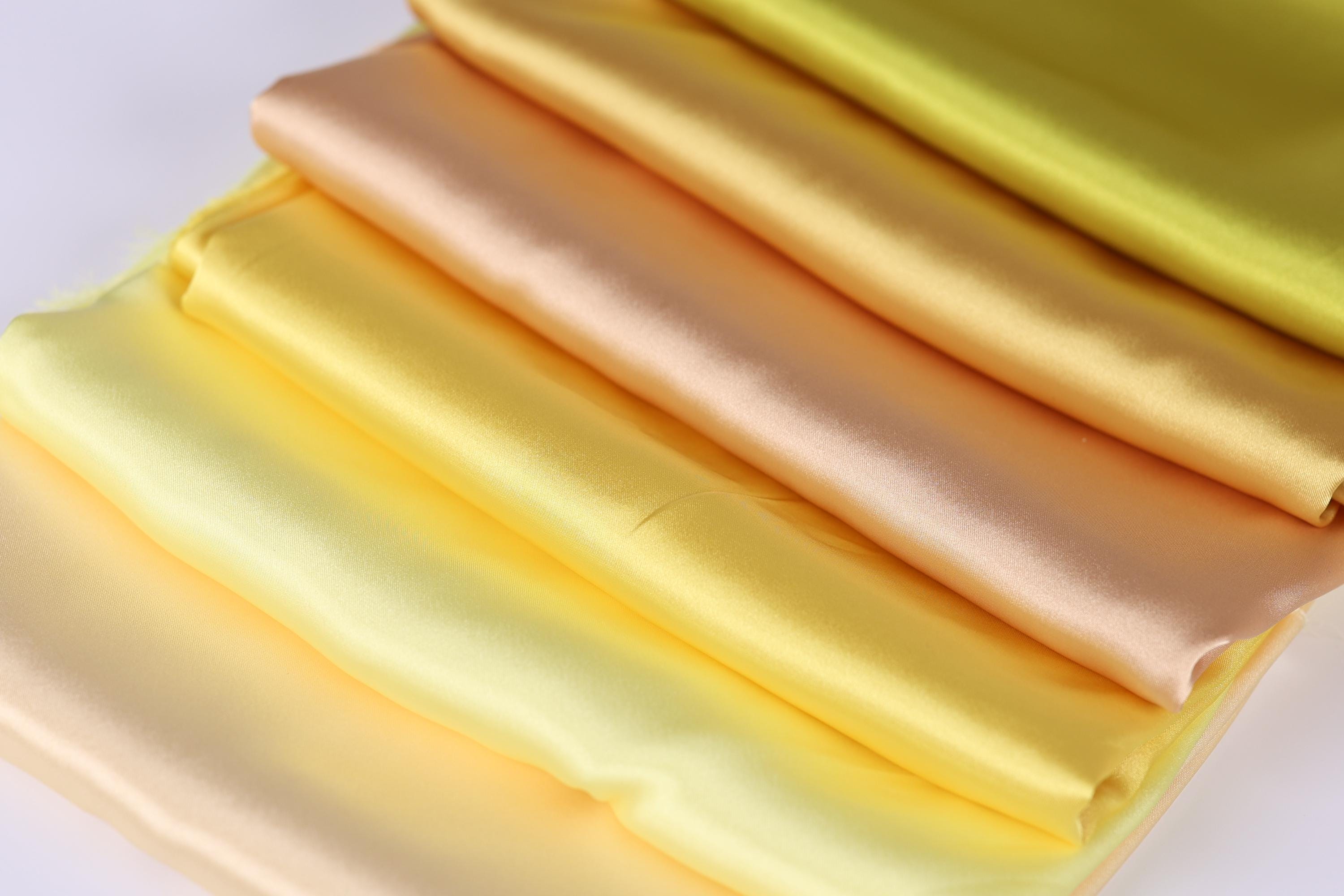 A close-up image of a stack of colorful fabric swatches, including yellow, orange, and peach hues.