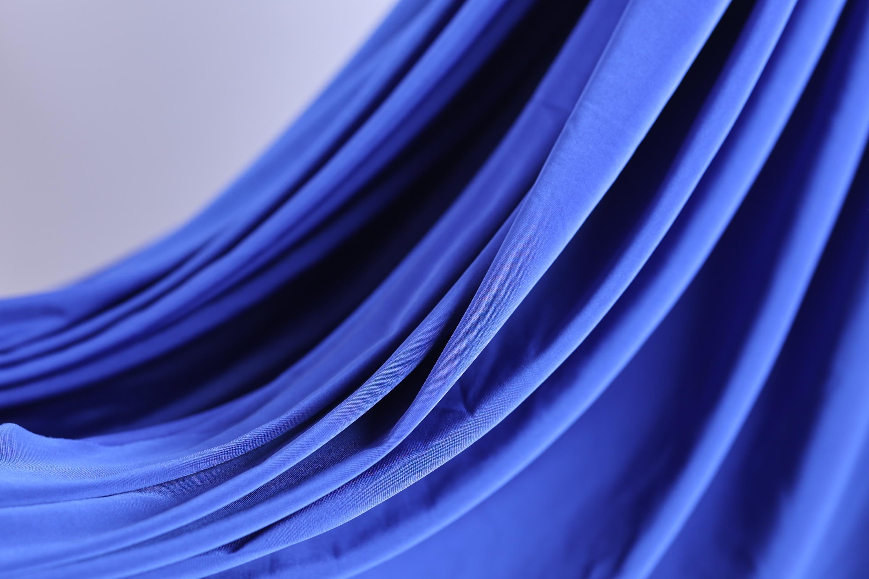 A close-up view of a blue fabric, possibly a curtain or garment, with a smooth, flowing texture.