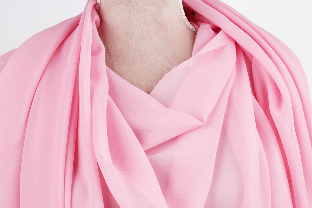 A close-up view of a pink fabric draped over a person's neck, with a necklace visible.