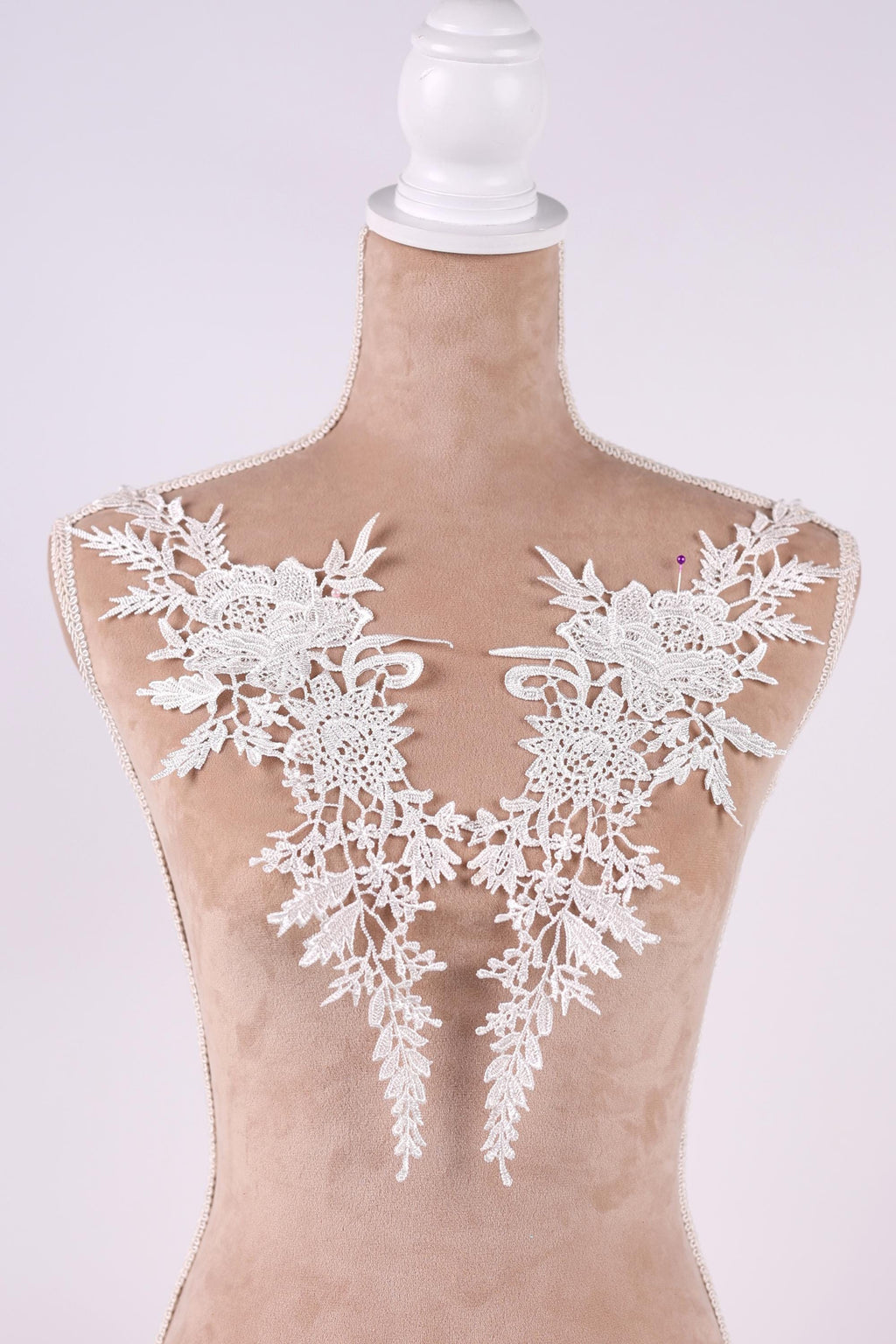 A mannequin wearing a white lace dress with intricate floral patterns on the shoulders.