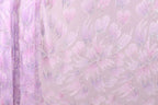 a close-up view of a fabric with a floral pattern in shades of pink and purple. The fabric appears to be made of a sheer material, with a delicate and intricate design. The pattern consists of numerous small flowers or petals, each with a unique shape and color, creating a visually appealing and textured appearance. The fabric is displayed against a light pink background, which further accentuates the vibrant colors and intricate details of the floral pattern.