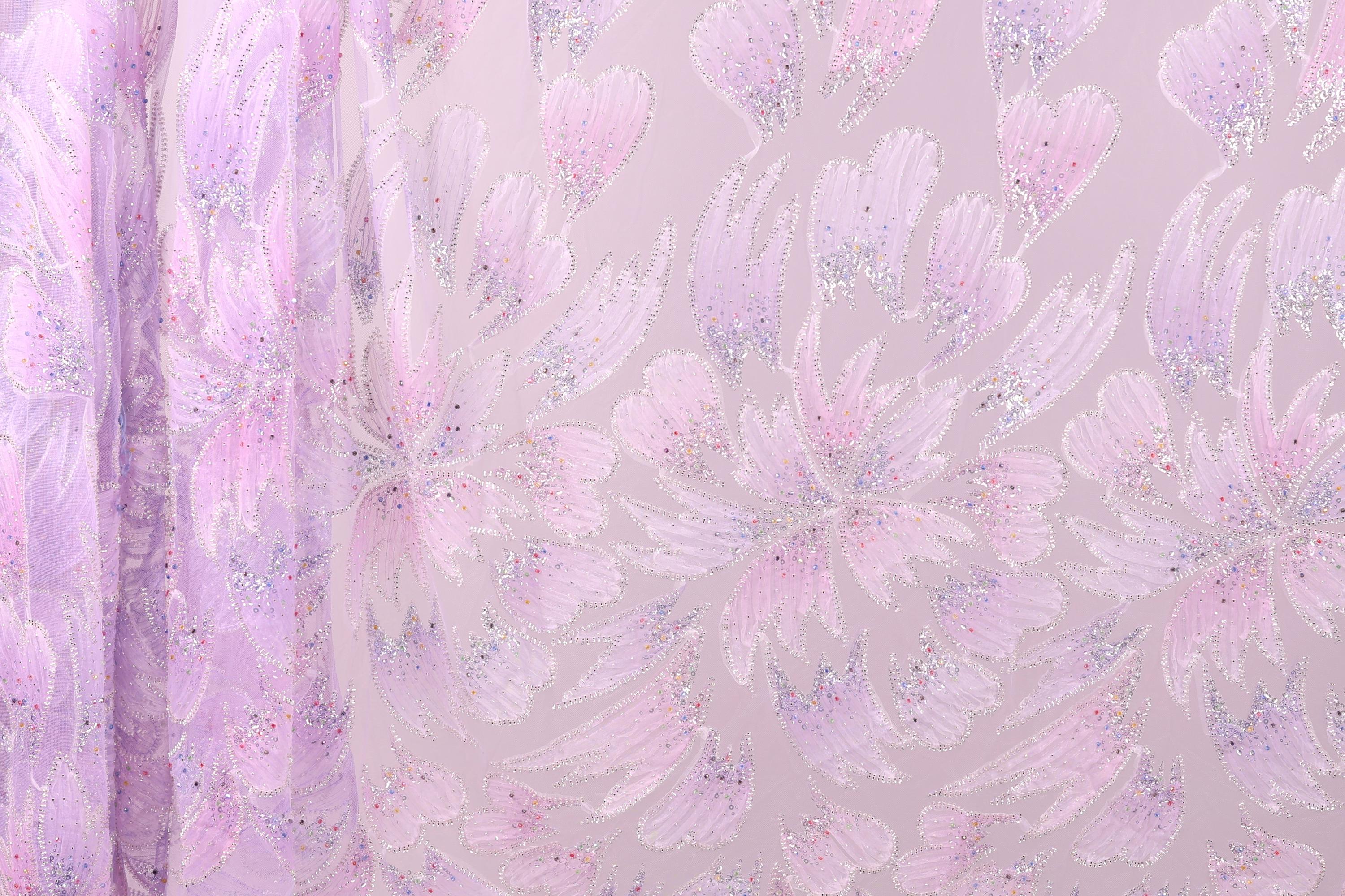 a close-up view of a fabric with a floral pattern in shades of pink and purple. The fabric appears to be made of a sheer material, with a delicate and intricate design. The pattern consists of numerous small flowers or petals, each with a unique shape and color, creating a visually appealing and textured appearance. The fabric is displayed against a light pink background, which further accentuates the vibrant colors and intricate details of the floral pattern.