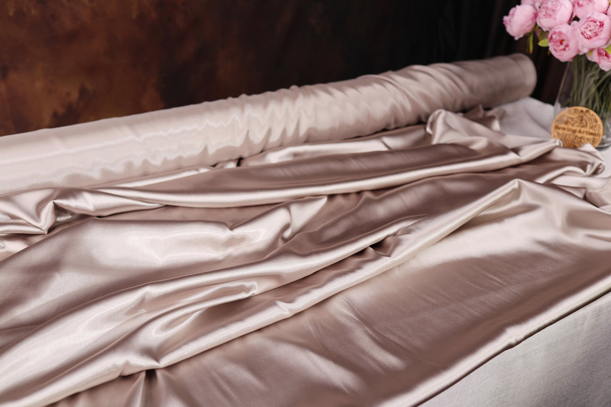 a close-up view of a crumpled, shiny fabric, possibly silk or satin, with a vase of pink flowers placed next to it.