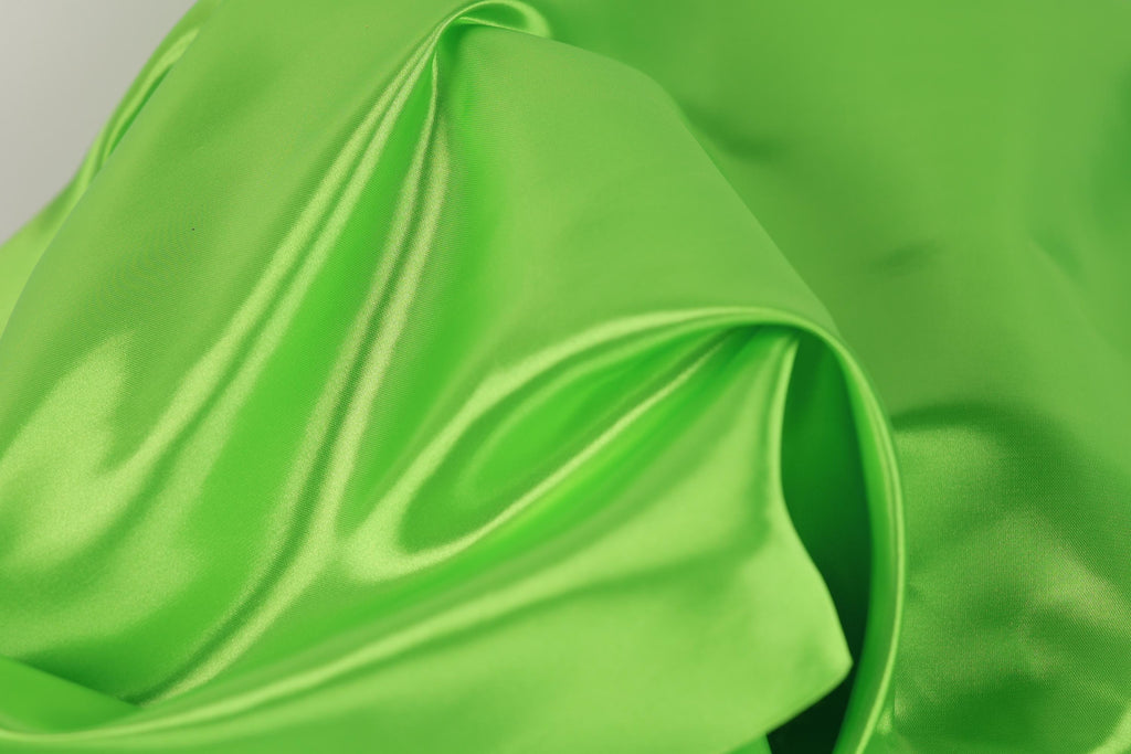 A close-up view of a bright green fabric, possibly silk or satin, with a smooth and shiny texture.