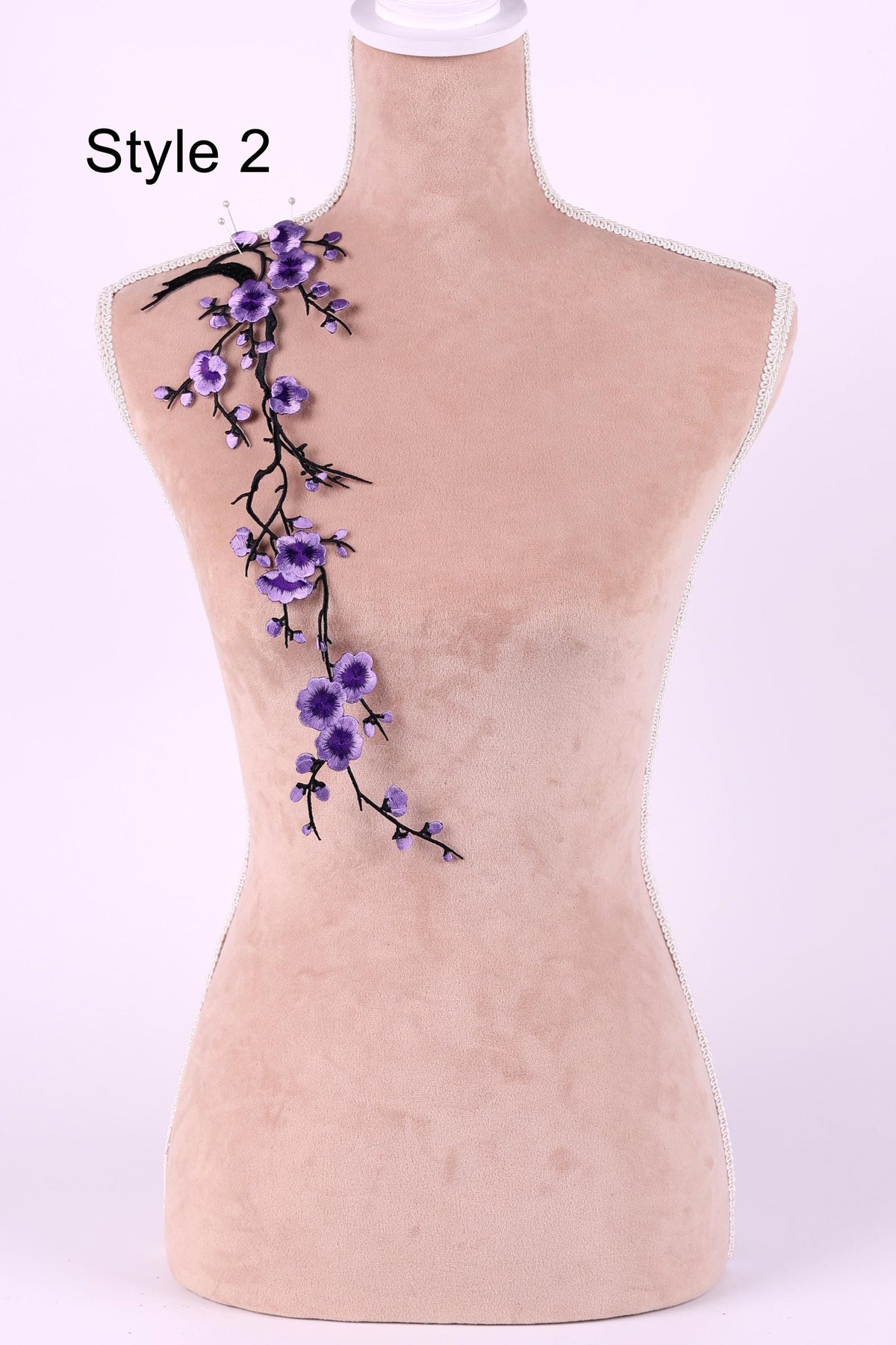 A mannequin with a floral design on its shoulder, featuring purple flowers and branches.