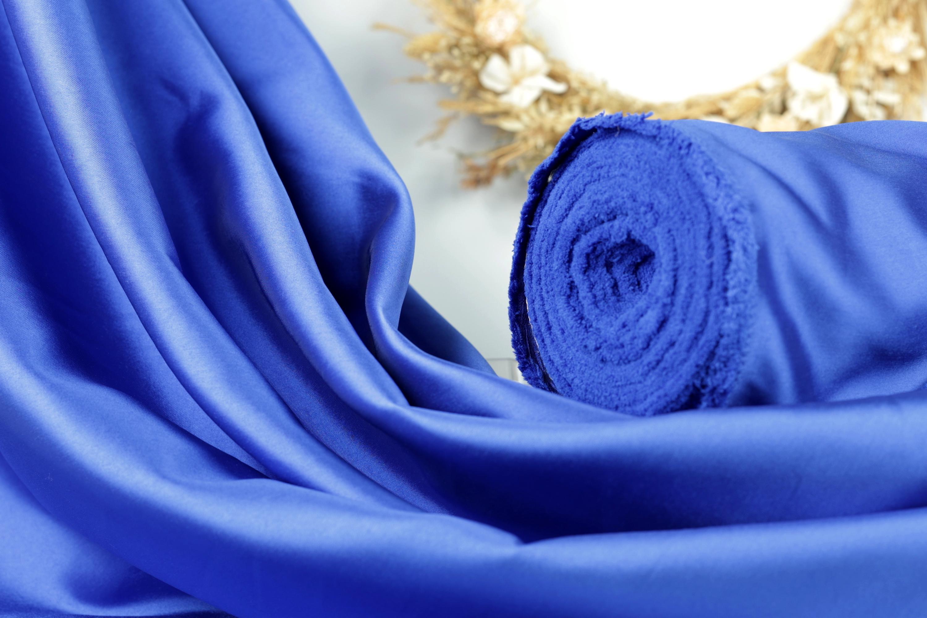 A close-up view of a blue satin fabric, with a rolled-up piece of the fabric visible in the background.