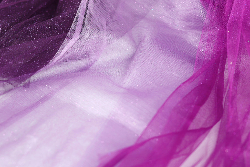 The image is a close-up of a fabric with a purple and white color scheme, featuring a textured and flowing appearance.