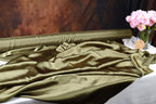 a roll of green satin fabric and a vase of pink flowers on a table.