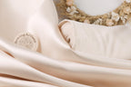 A close-up image of a white fabric with a label that reads "SewingArtisan" on it, along with a wreath made of dried flowers in the background.