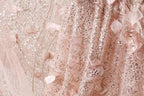 The image is a close-up of a delicate, pink, and beige fabric with intricate details, including sequins and lace-like patterns.