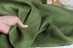 A hand is holding a piece of green fabric, which appears to be made of linen.