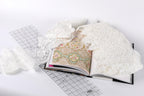 an open book with a lace pattern on the cover, lying on a white surface. There is also a piece of white lace and a ruler visible in the scene.