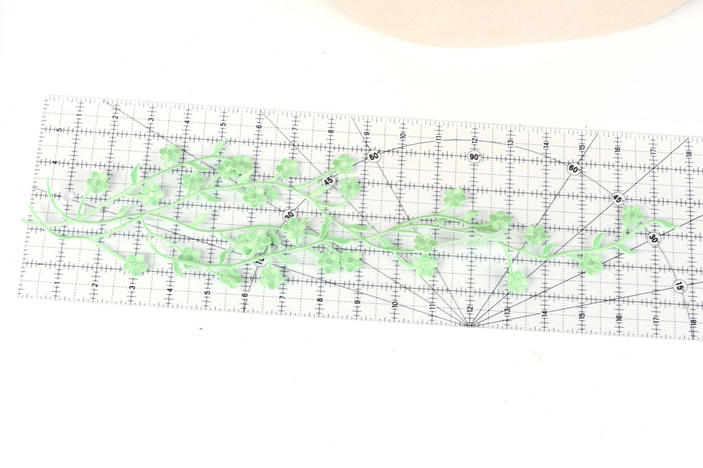 a clear ruler with green leaves and stems placed on it, indicating a measurement or design process.