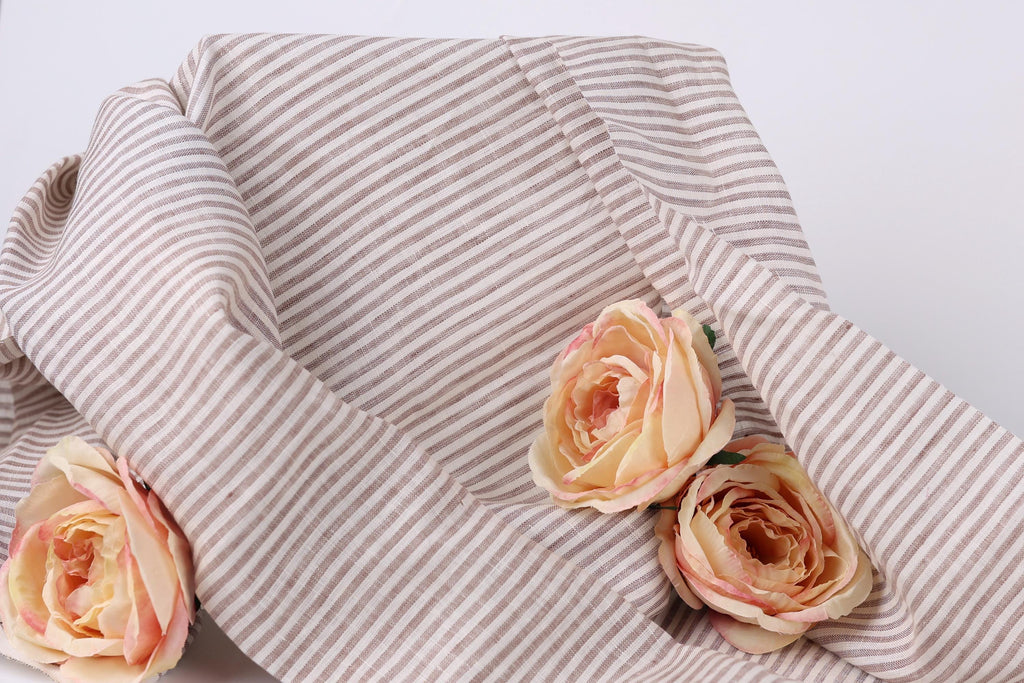 A close-up view of a beige and white striped fabric with three delicate pink roses resting on it.