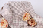 A close-up view of a beige and white striped fabric with three delicate pink roses resting on it.