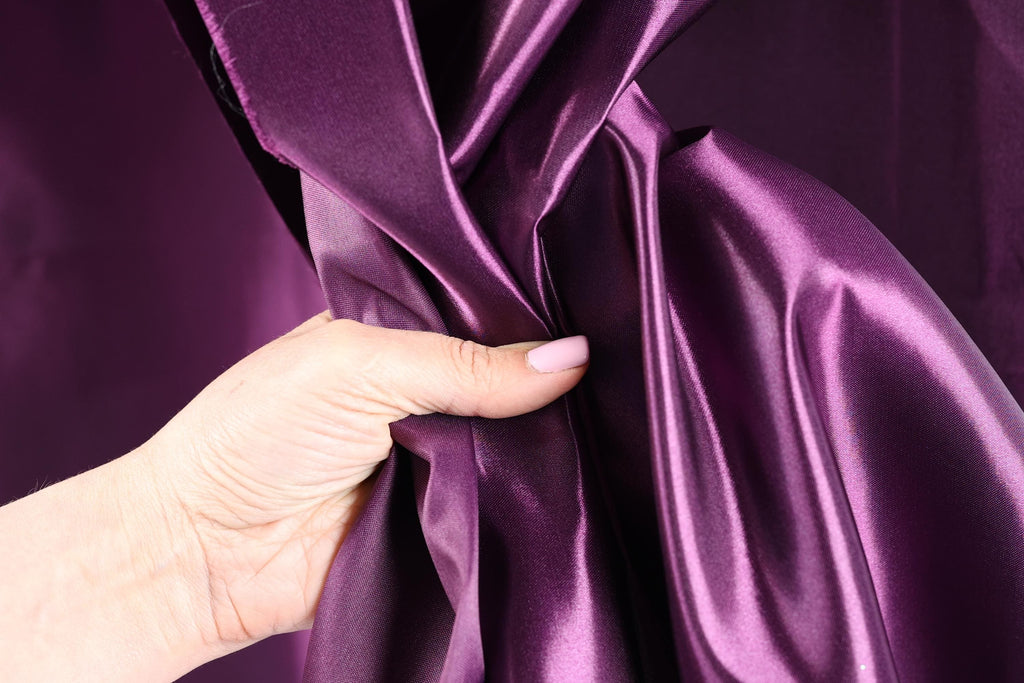 A hand is holding a purple satin fabric, with the fabric partially draped over the hand.