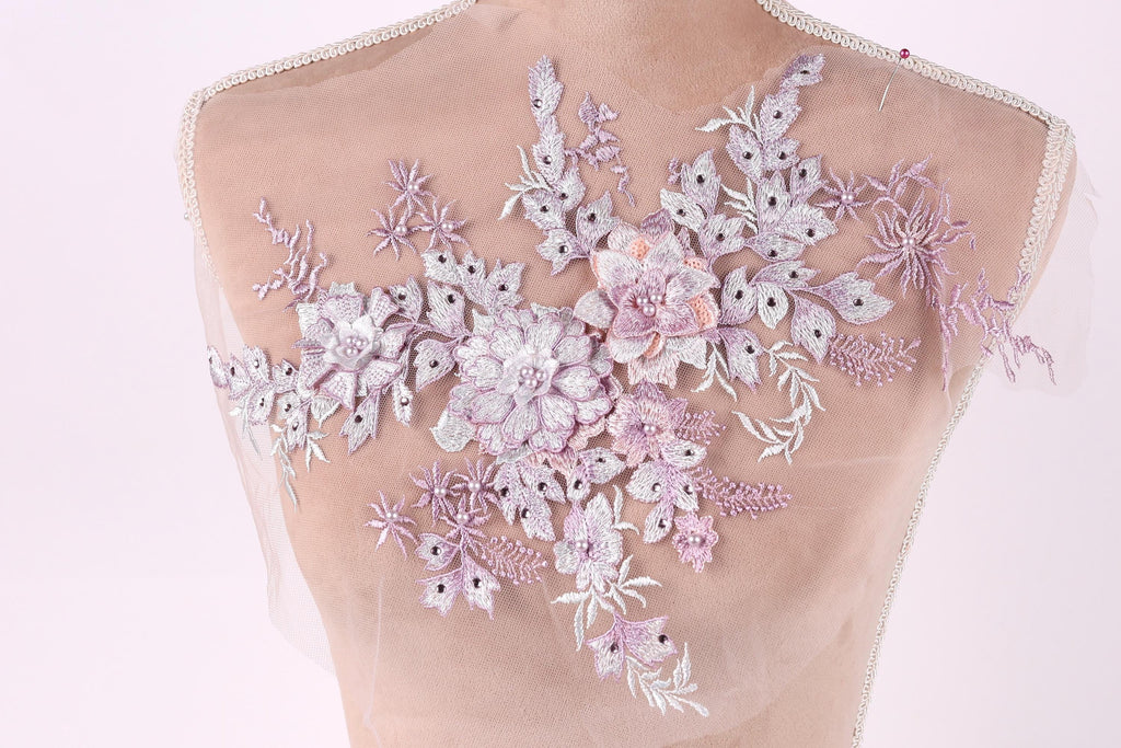 a delicate and intricate floral embroidery design on a mannequin or dress form, showcasing a variety of pink and white flowers and leaves.