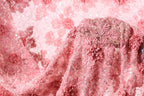 a close-up view of a delicate, pink fabric with intricate floral designs. The fabric appears to be made of lace or a similar delicate material, with a floral pattern that includes pink flowers and leaves. The fabric is draped over a surface, creating a visually appealing and elegant display.