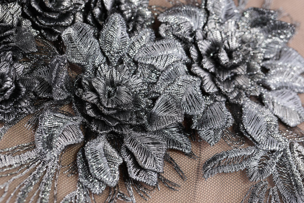 a close-up view of a delicate, metallic fabric with intricate, metallic flower-like patterns. The fabric appears to be made of a shiny, metallic material, giving it a metallic, metallic-looking appearance. The close-up perspective allows for a detailed view of the fabric's texture and design.