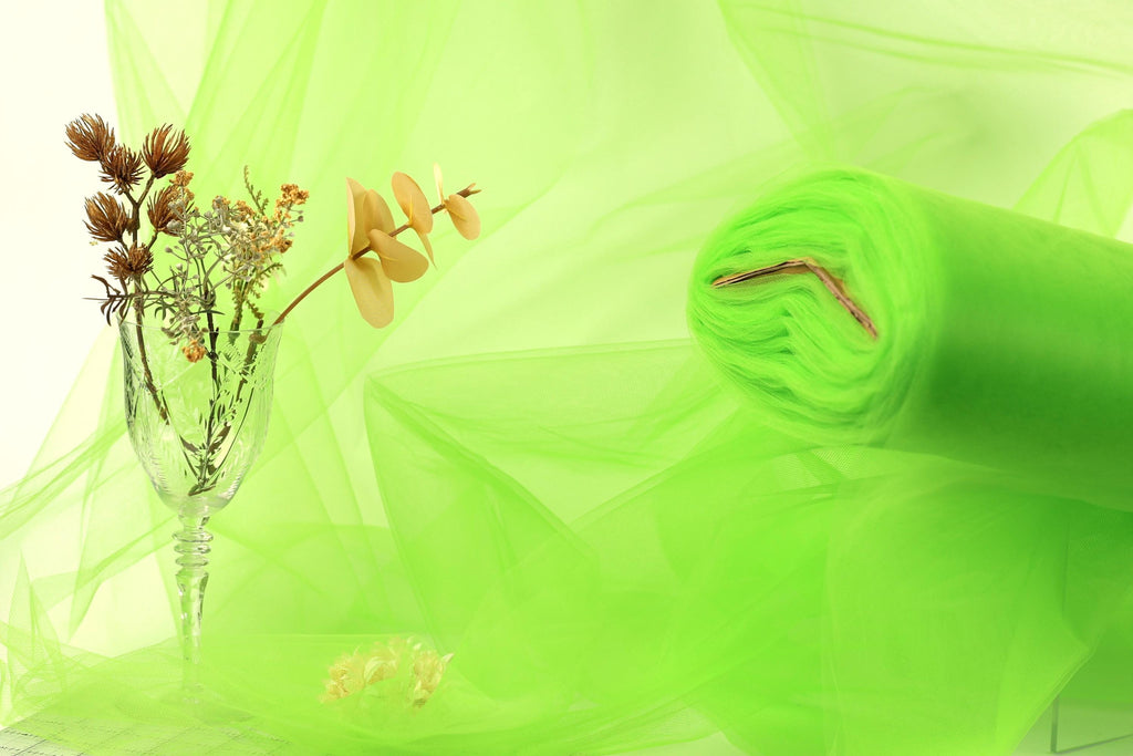 a glass vase with flowers, a rolled-up green fabric, and a blurred green background.
