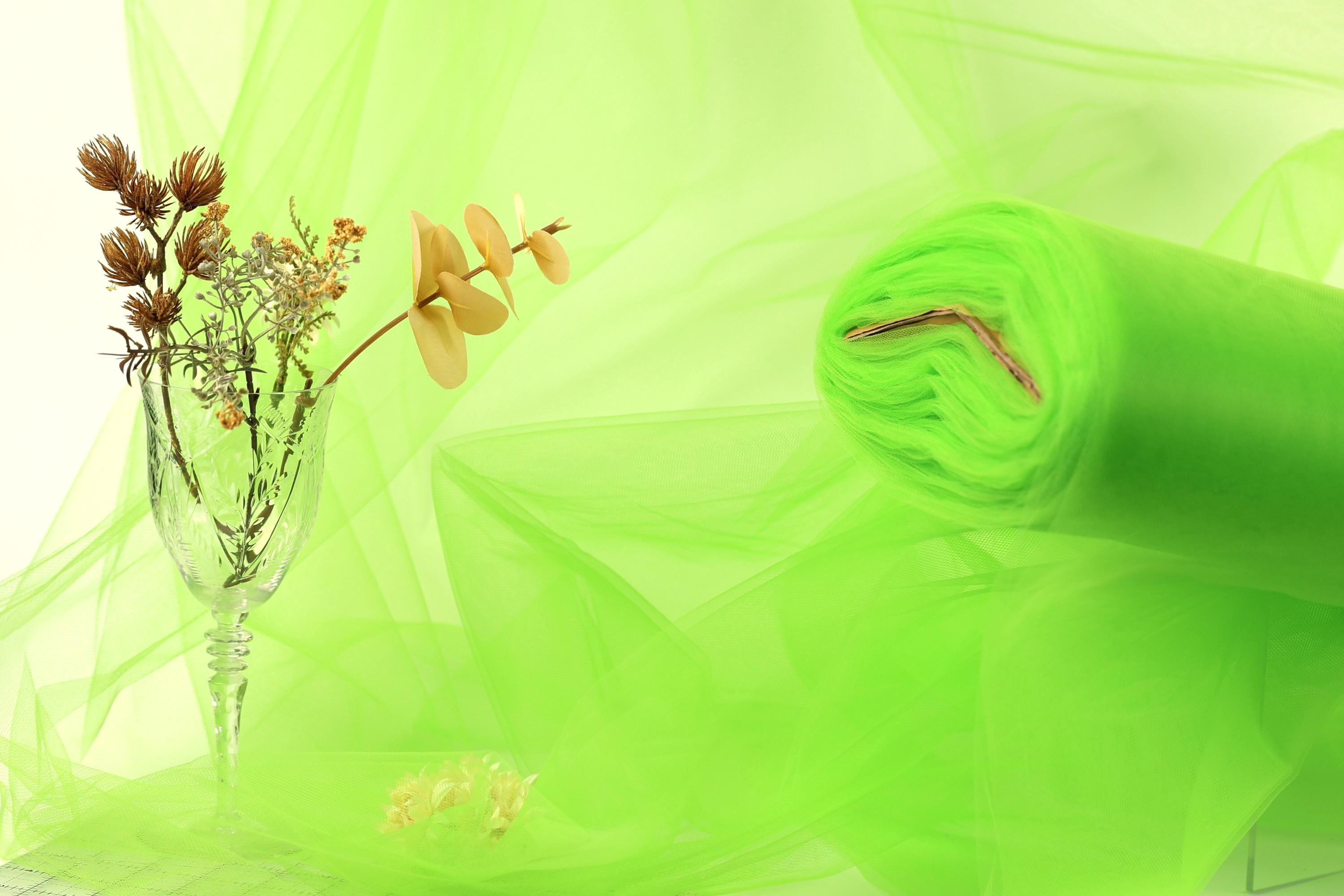 a glass vase with flowers, a rolled-up green fabric, and a blurred green background.