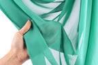 A hand is holding a piece of green fabric, which appears to be a sheer material.