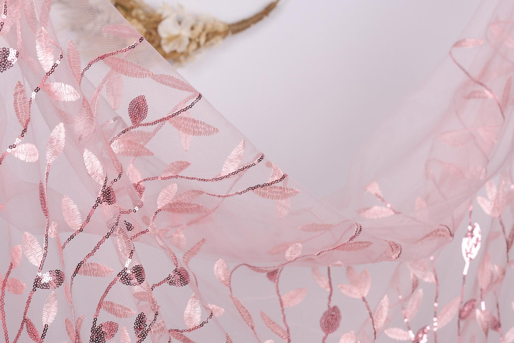 a close-up view of a delicate, pink, and white floral-patterned fabric, possibly a sheer or sheer lace material. The fabric appears to be made of sheer material, with a delicate and intricate design of leaves and flowers. The image does not contain any text or other discernible objects, and the focus is solely on the fabric's texture and pattern.