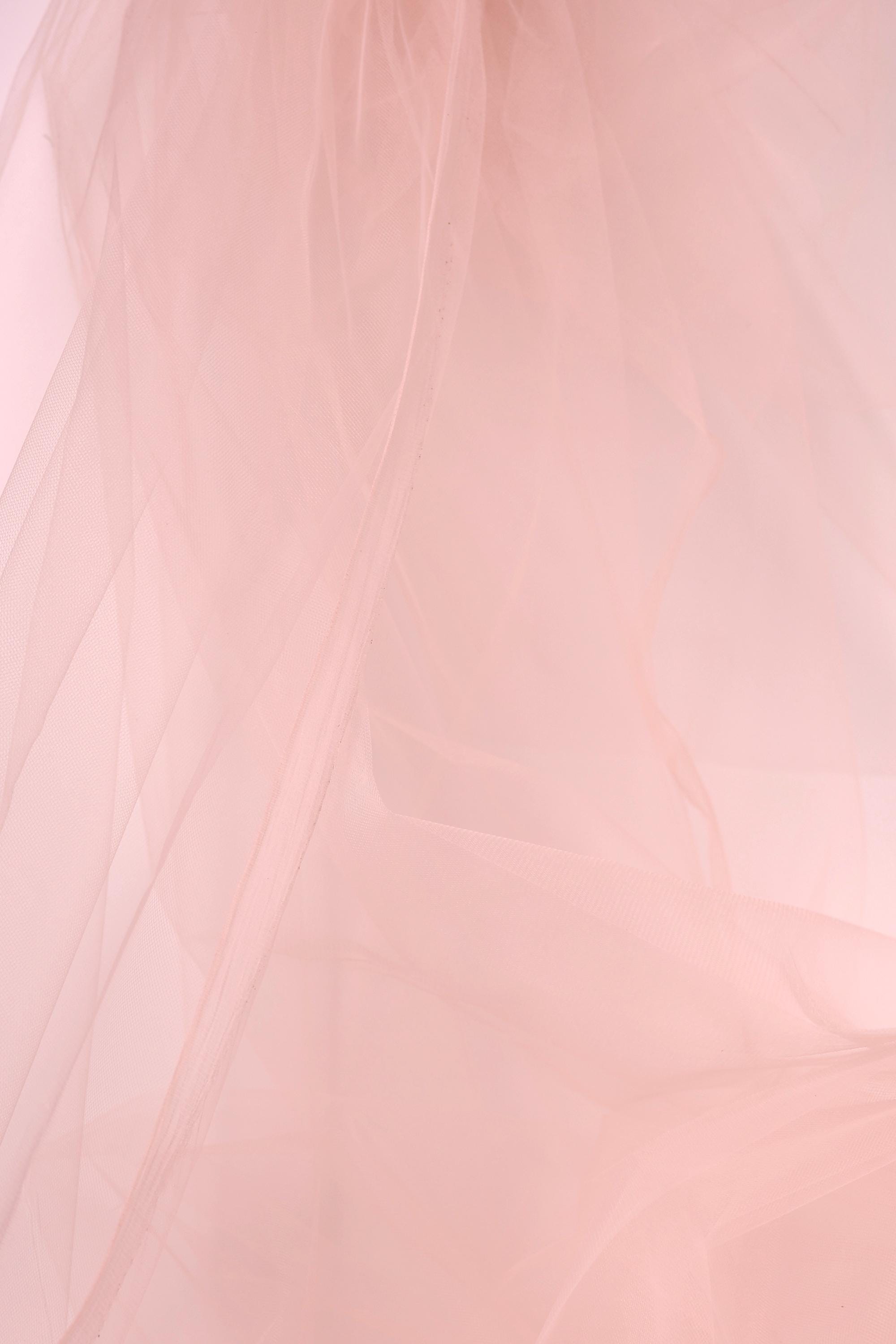 The image is a close-up of a soft, light pink fabric, possibly tulle, with a slightly wrinkled texture.