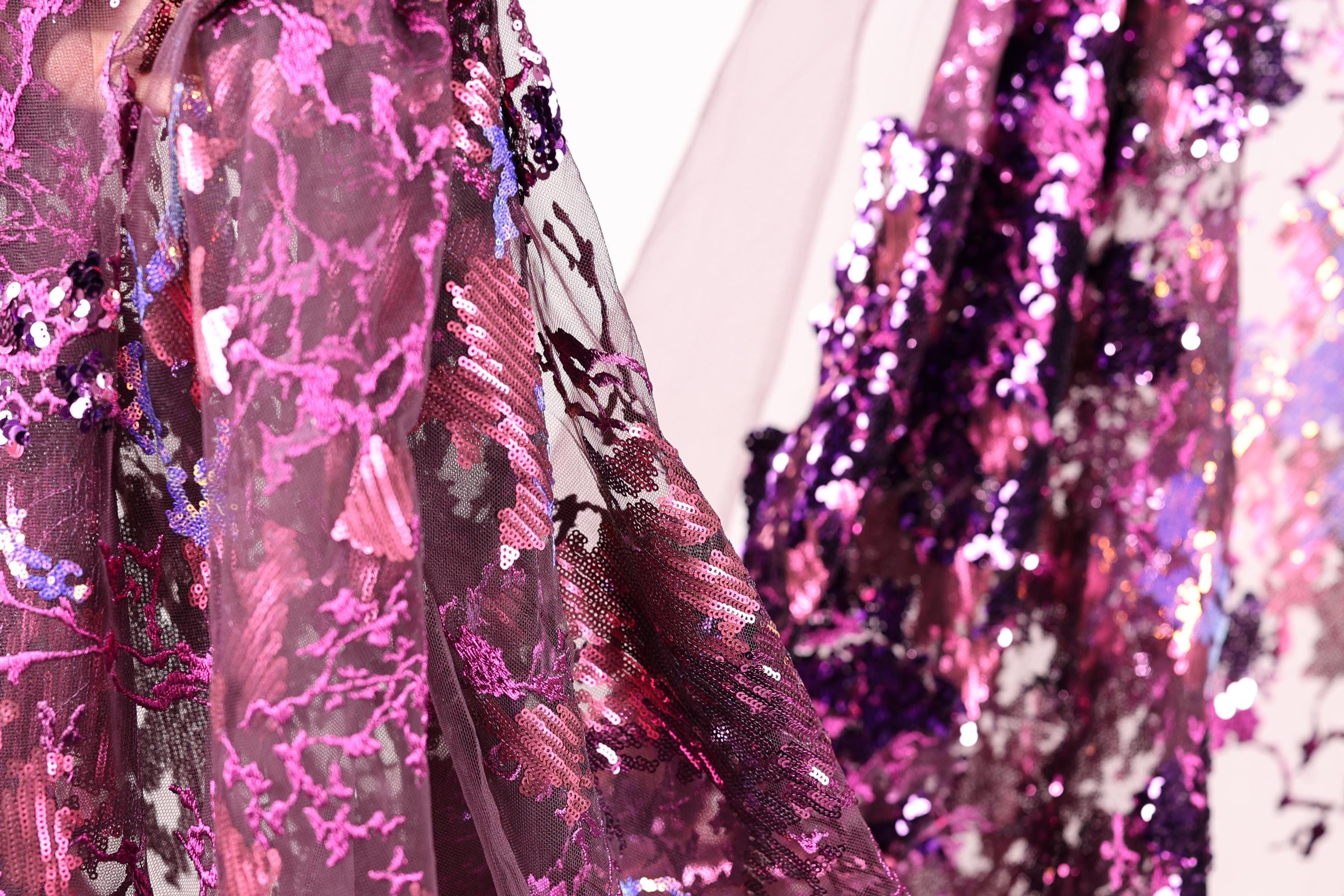 a close-up view of a fabric with a vibrant, multicolored pattern, including shades of pink, purple, and blue. The fabric appears to be made of sequins or other embellishments, adding a touch of sparkle and glamour to the design.