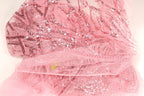 The image is a close-up of a pink sequin fabric with a delicate, intricate pattern.