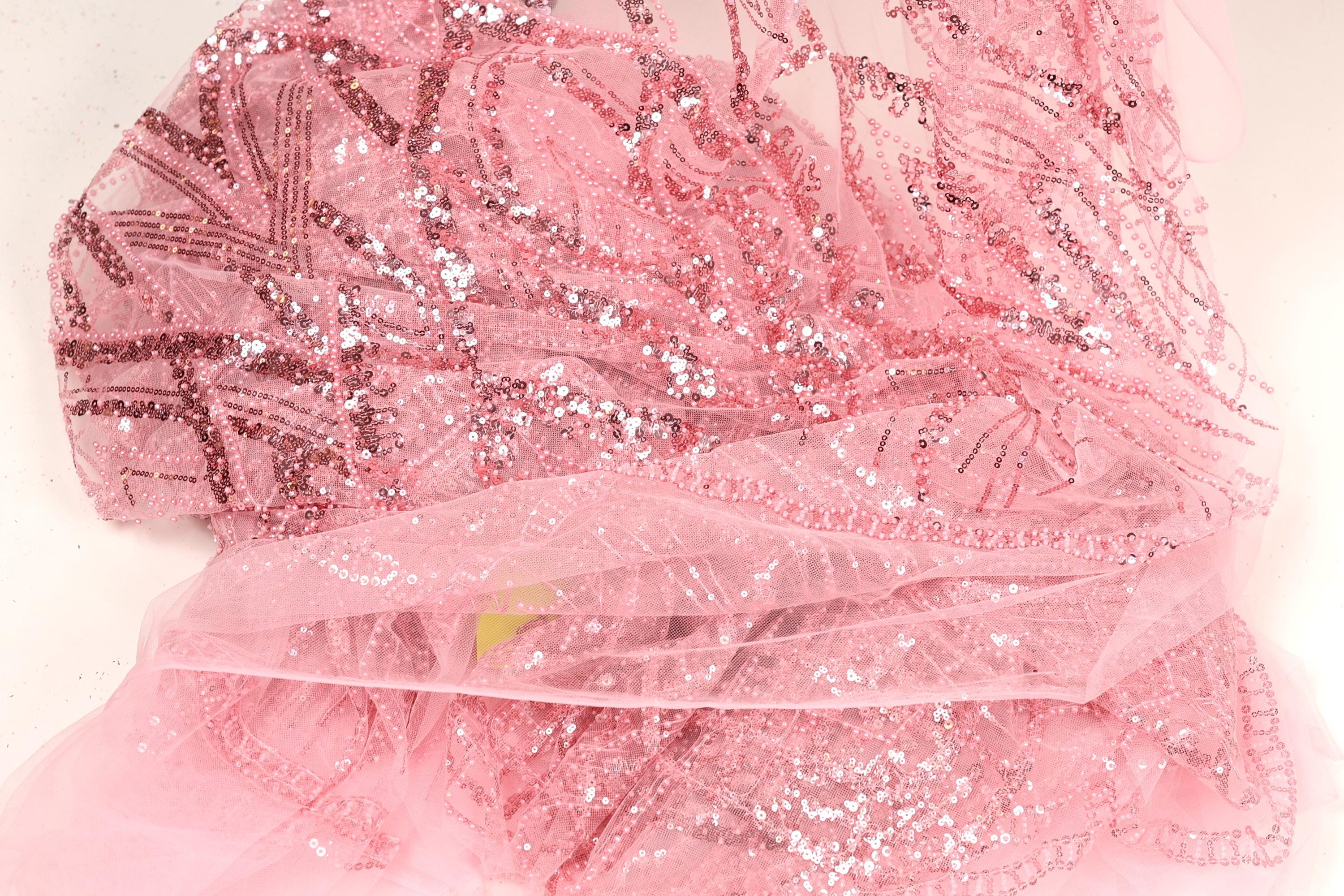 The image is a close-up of a pink sequin fabric with a delicate, intricate pattern.