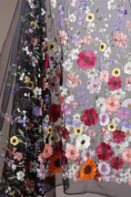 a close-up view of a fabric with a floral pattern, showcasing a variety of colorful flowers such as red, pink, yellow, and white. The fabric appears to be a sheer material, with the flowers intricately embroidered or printed onto it, creating a visually striking and vibrant design.