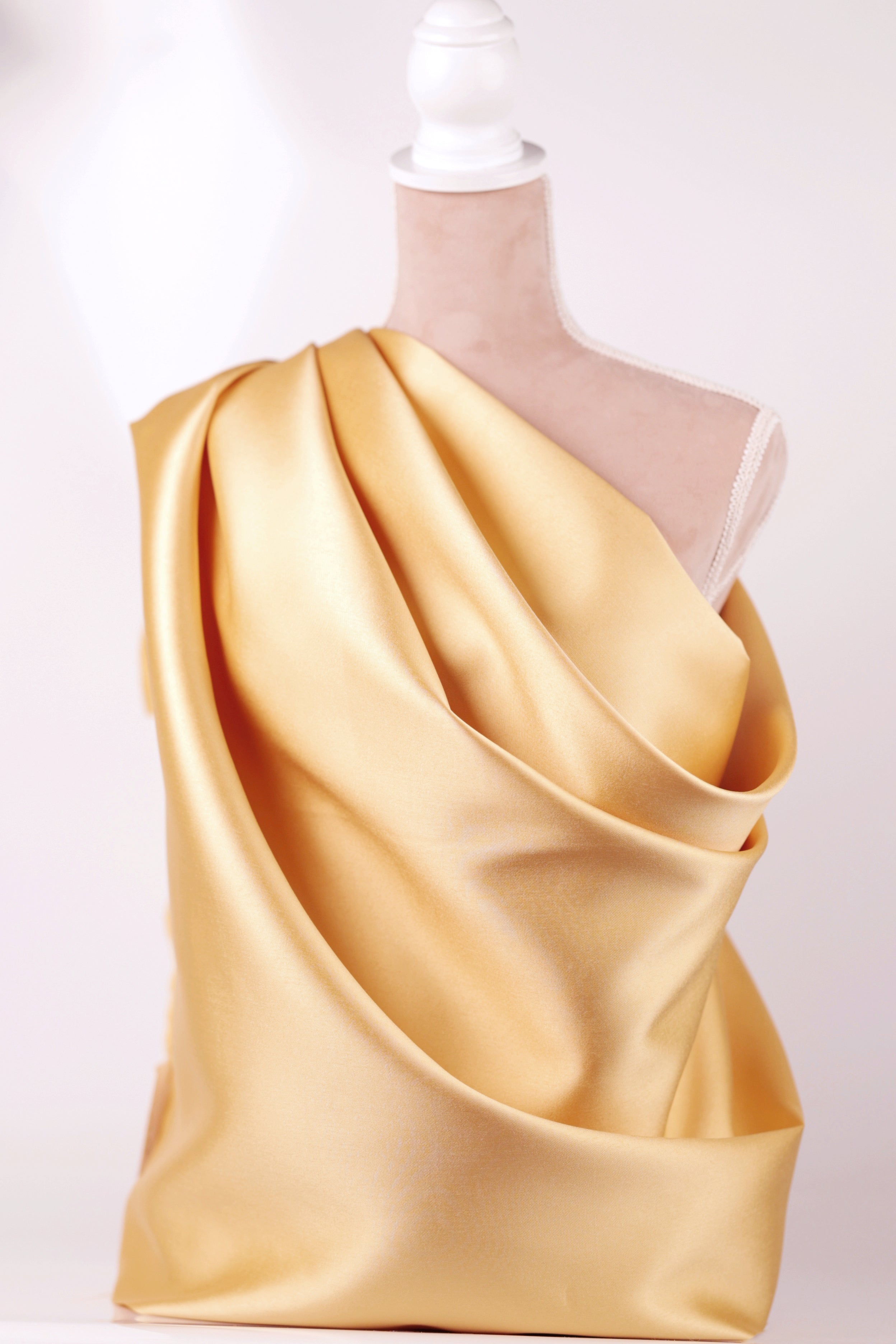 A mannequin wearing a gold satin one-shoulder dress with a draped, flowing silhouette.