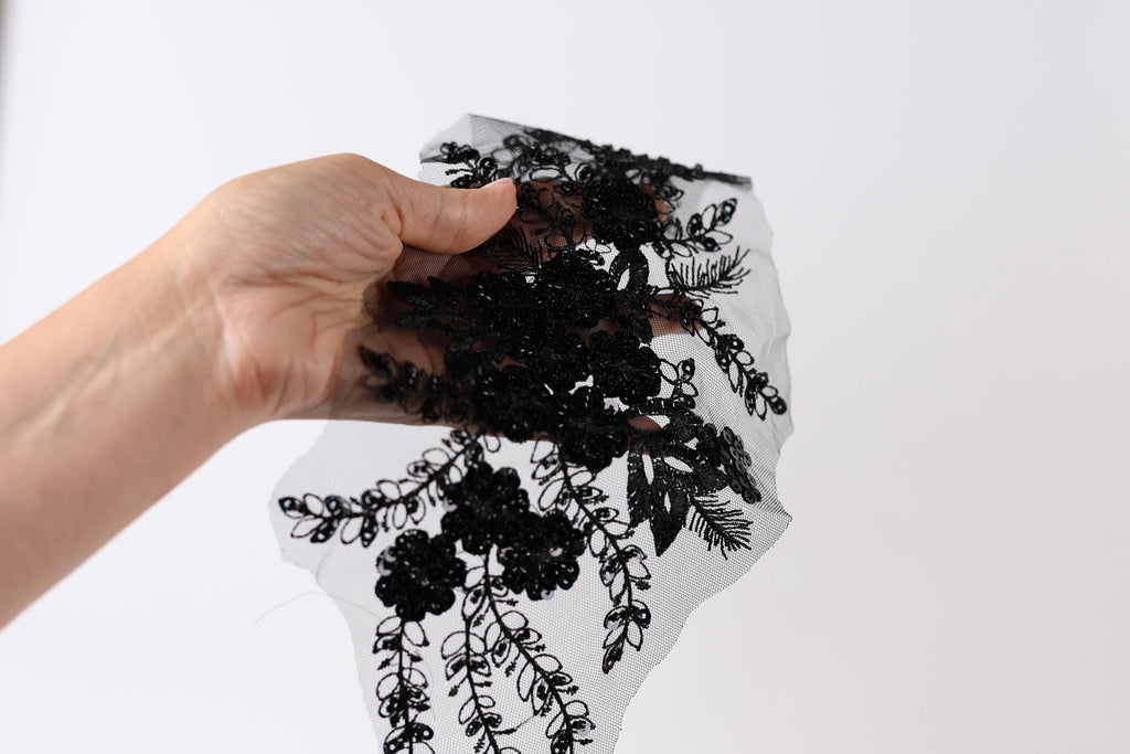 A hand is holding a piece of black fabric with a floral pattern, against a white background.