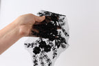 A hand is holding a piece of black fabric with a floral pattern, against a white background.