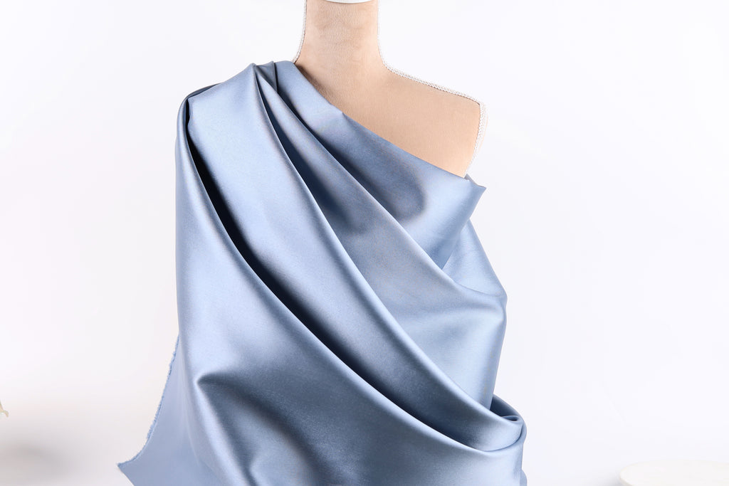 A mannequin wearing a blue satin fabric draped over its shoulder.