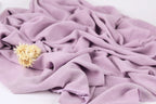 A close-up image of a crumpled, purple fabric with a single yellow flower resting on it.