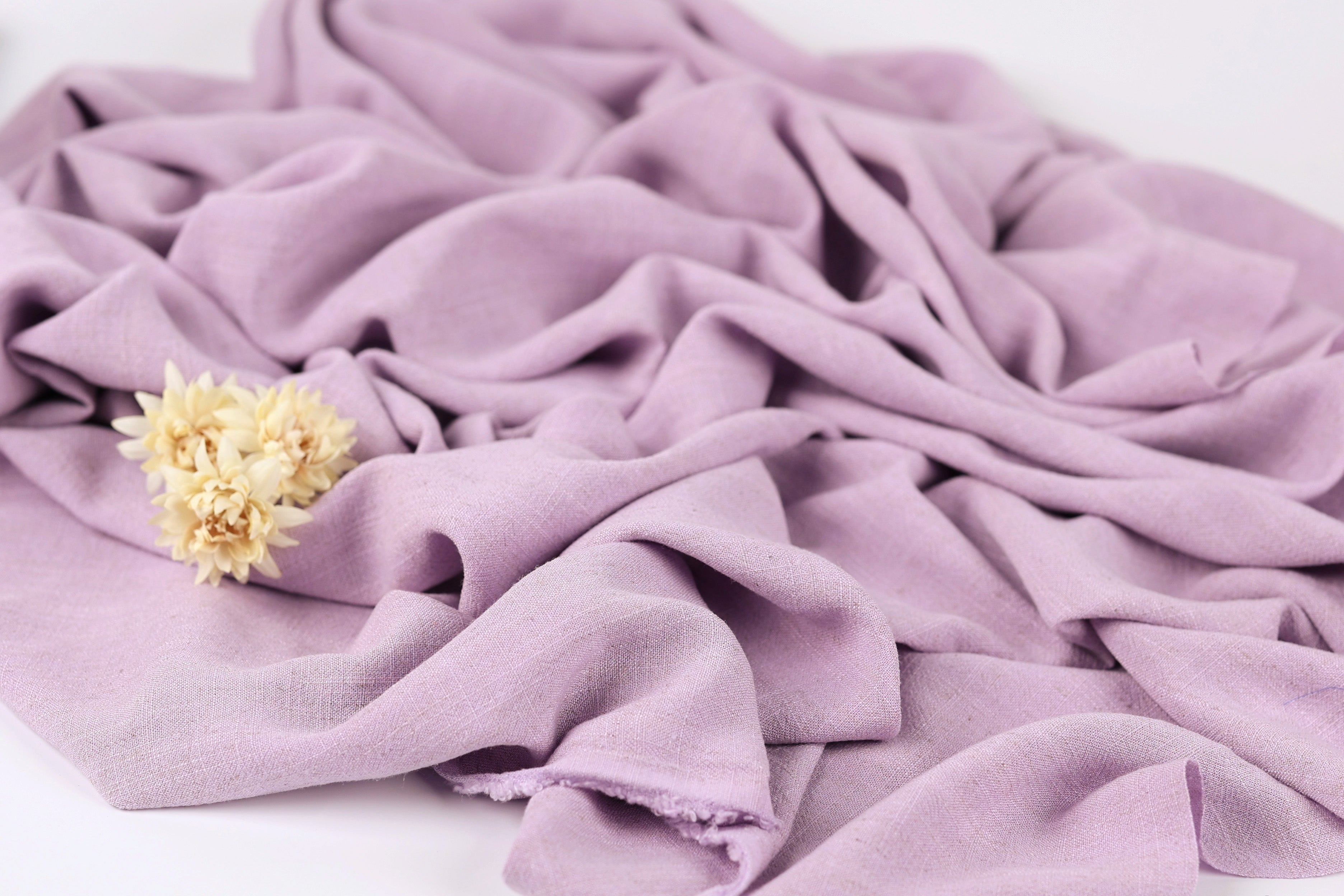 A close-up image of a crumpled, purple fabric with a single yellow flower resting on it.