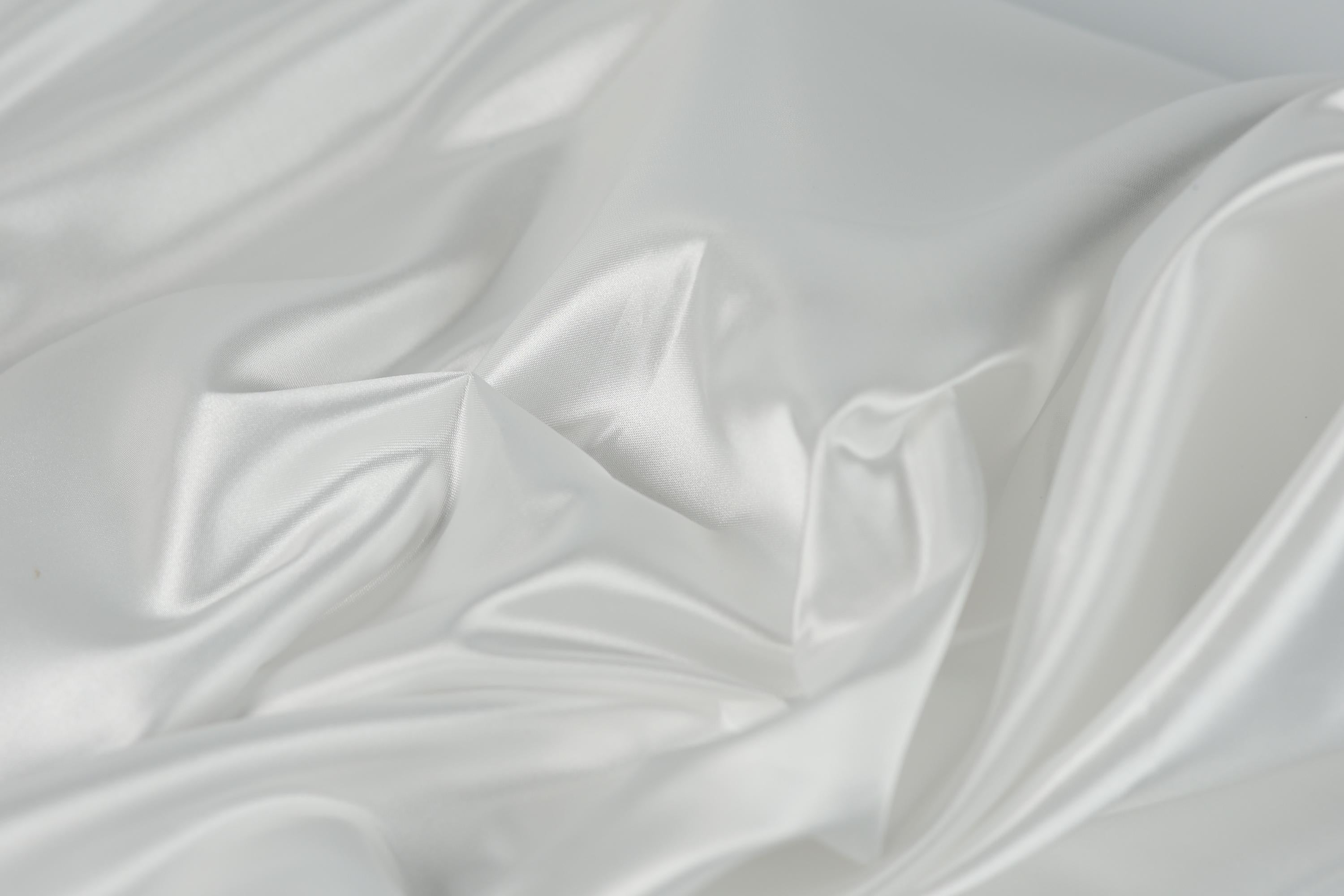 The image is a close-up of a white, flowing fabric, possibly silk or satin, with a soft, shiny texture.