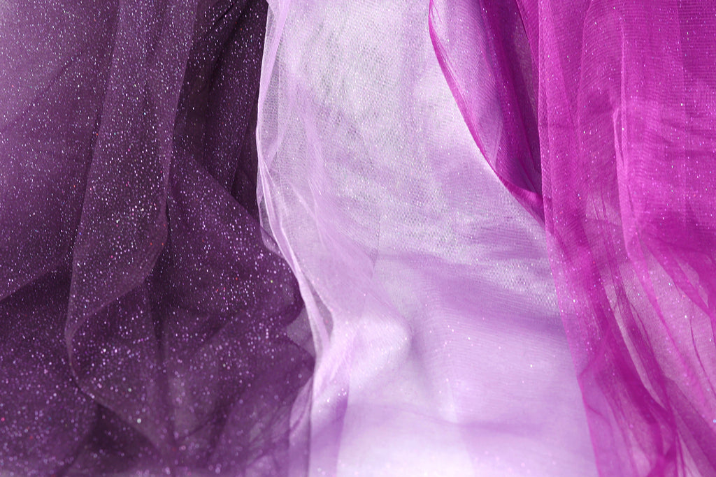 a close-up view of a fabric with a purple and white color scheme, featuring a shiny, glittery texture.