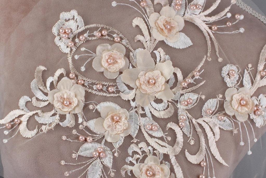 a close-up view of a delicate, intricate floral embroidery design on a fabric surface. The design is composed of numerous small flowers, leaves, and pearls, creating a visually appealing and detailed pattern. The flowers are arranged in a way that they appear to be growing out of the fabric, adding a sense of depth and complexity to the overall design. The image does not contain any text or other discernible objects, and the focus is solely on the intricate floral embroidery.