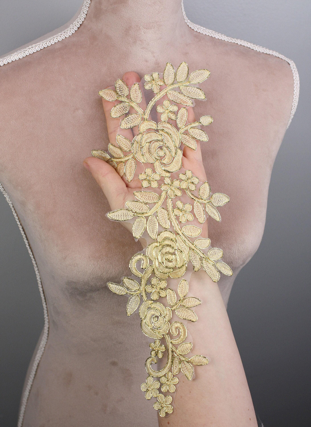 A mannequin torso wearing a gold floral lace piece on its arm.