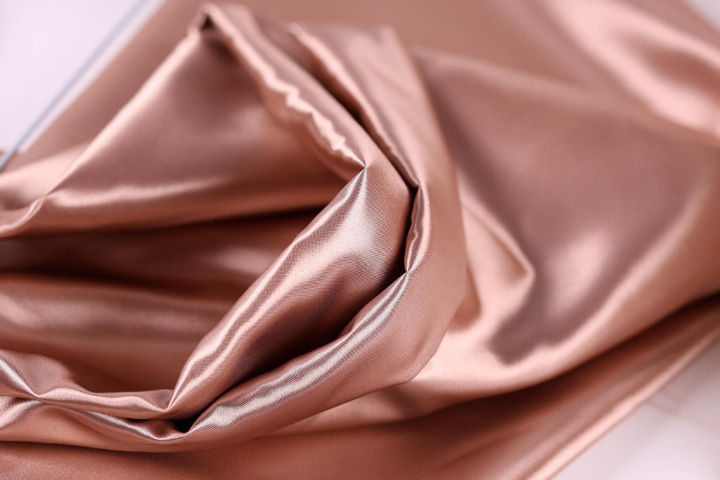 A close-up view of a soft, shiny, and smooth fabric, possibly silk or satin, with a rich, warm color palette.