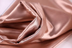 A close-up view of a soft, shiny, and smooth fabric, possibly silk or satin, with a rich, warm color palette.