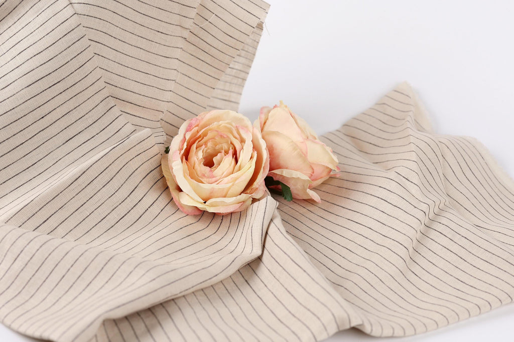 Two delicate pink roses resting on a beige fabric with black stripes.